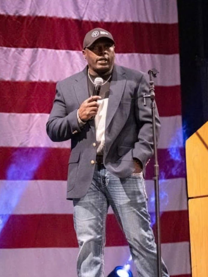 Jonathan Harvey host of The Modern Conservative Podcast speaking with the American Flag behind him.